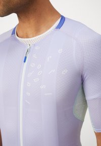Maillot de cyclisme violet avec une fermeture éclair sur le devant, des panneaux en mesh et un tissu texturé. Présente des accents bleu clair et un texte imprimé sur le devant.