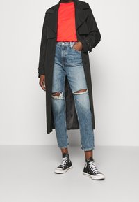 Svart trenchcoat, röd T-shirt, slitna blå jeans och svarta högstövlar. Har knappar och en lång, flödande design.