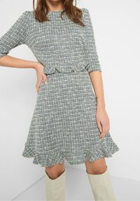 Sininen ja valkoinen ruudullinen mekko, jossa on kolmivartiset hihat, liehuva helma ja röyhelödetaljilla varustettu vyötärö, valmistettu teksturoidusta kankaasta.