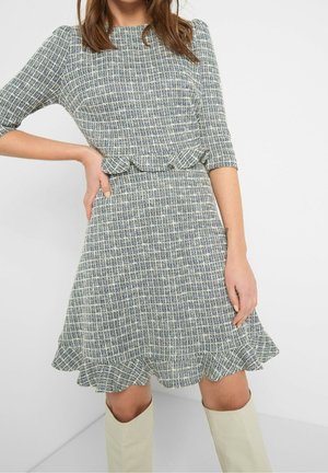 Robe à carreaux bleus et blancs avec des manches trois-quarts, un ourlet évasé et des détails à volants à la taille, en tissu texturé.