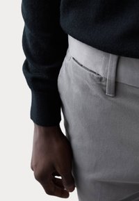 Pantaloni in cotone grigi con una texture liscia, caratterizzati da un frontale piatto e tasche laterali, abbinati a un maglione nero in maglia.