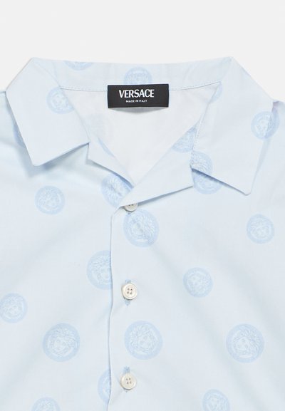 Svetlo modra srajca s kratkimi rokavi iz bombaža, z vzorcem krožnih medaljonov, vsak z obrazom, in belimi gumbi.