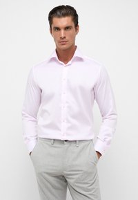 Lichtroze overhemd met een gestructureerde kraag, knoopsluiting aan de voorkant en lange mouwen. Gladde textuur; gedragen met grijze broek.