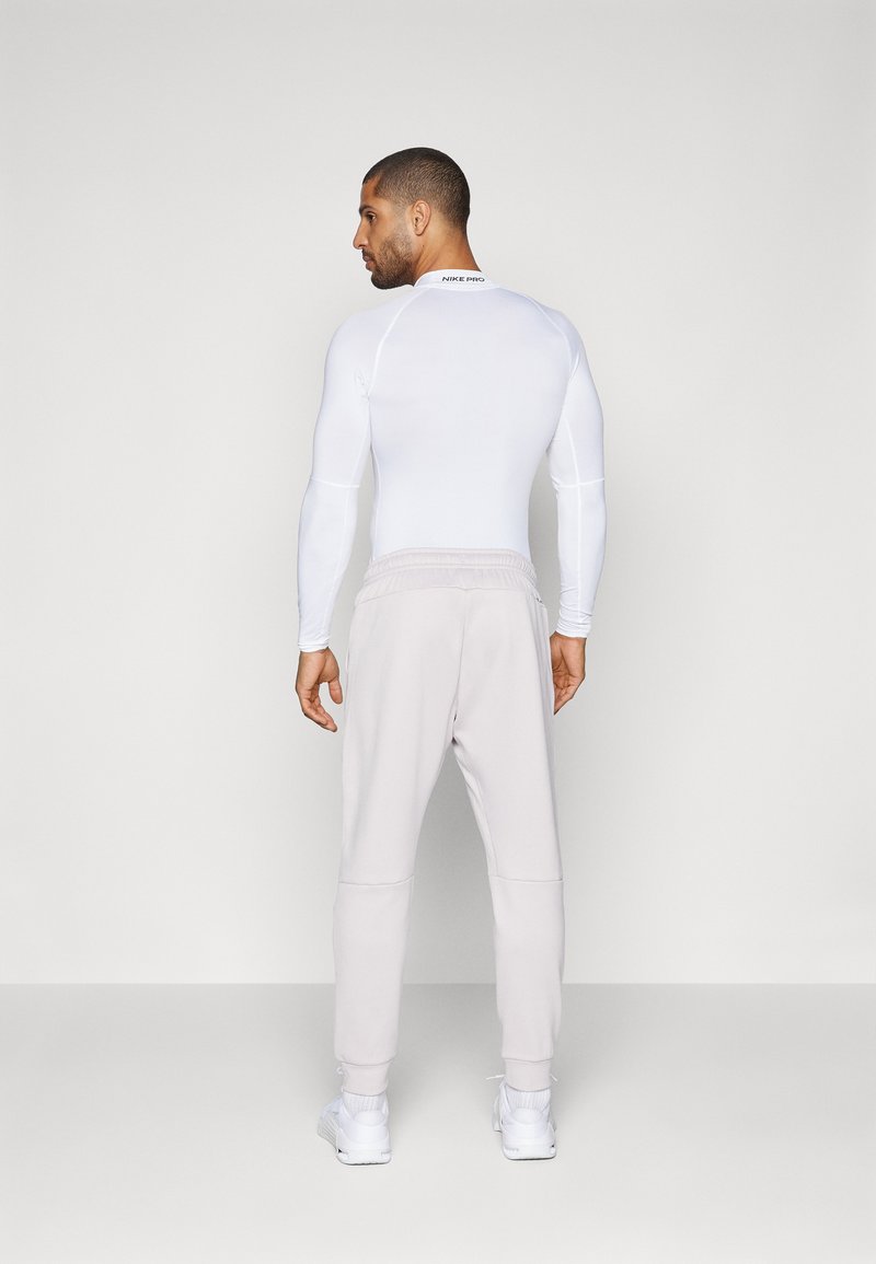Haut de sport à manches longues blanc et joggers gris clair. Le haut est en tissu extensible ; les joggers ont une taille élastique et des ourlets resserrés. Baskets blanches.