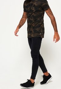 Černé camo tričko s krátkým rukávem, s výrazným logem. V kombinaci s černými skinny džíny a černými sportovními botami.