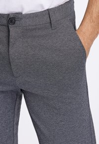 Grijze broek gemaakt van getextureerde stof met een knoopsluiting aan de tailleband, voorzien van zijzakken en een getailleerde pasvorm.