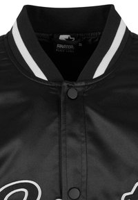 Blouson aviateur en satin noir avec un col côtelé, deux rayures blanches, une fermeture à boutons et un texte brodé à l'avant.