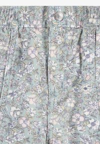 Gros plan d'un tissu avec un motif floral pastel en verts doux, roses et blancs, avec un bouton en métal argenté et des coutures cousues.