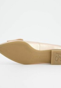 Nude nahka slipperit, joissa on pyöreä kärki ja matala, beige pohja. Sisältää hienovaraisia ompeleita ja pienen ommellun yksityiskohdan päällisessä.