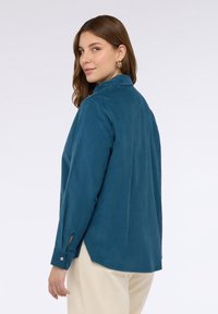 Turkusowa koszula z guzikami, z kołnierzykiem, długimi rękawami, bocznymi rozcięciami oraz złotymi akcentami na mankietach, zaprojektowana z miękkiego, strukturalnego materiału.