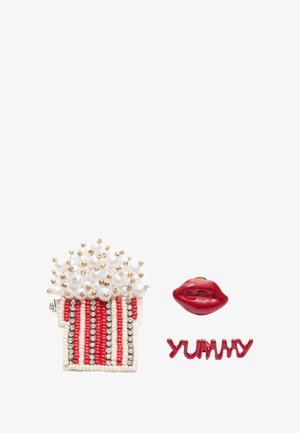 Brož s popkornem z perličkami, s červenobílými pruhy, zdobenými bílými perličkami a zlatými akcenty; obsahuje červené rty a text "YUMMY" v červené barvě.