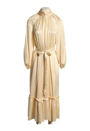 Robe midi beige clair à manches longues avec col montant, taille nouée, pois subtils et ourlet à volants sur un mannequin simple.
