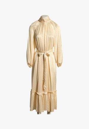 Robe midi beige clair à manches longues avec col montant, taille nouée, pois subtils et ourlet à volants sur un mannequin simple.