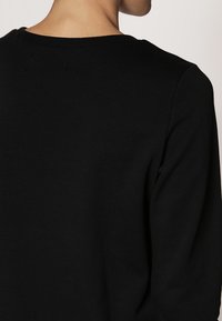 Černý svetr s kulatým výstřihem a dlouhými rukávy, vyrobený z jemného materiálu s hladkou texturou, zobrazený zezadu.