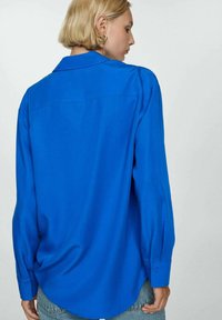 Camicia azzurra a maniche lunghe con colletto e polsini abbottonati, caratterizzata da una superficie liscia, una vestibilità comoda e un orlo arrotondato.
