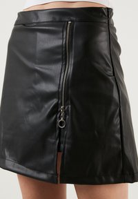 Fustă din piele ecologică neagră cu un finisaj lucios, având un fermoar lateral cu accesorii argintii și un tiv drept.