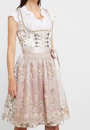 Une femme porte un dirndl brodé rose pâle, avec un chemisier blanc en dentelle, un corsage fleuri et un ruban de satin noué à la taille.