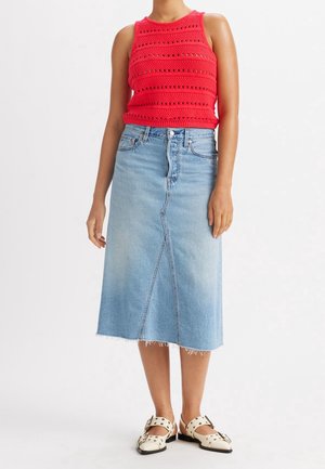 Haut sans manches en tricot rouge avec des motifs horizontaux, associé à une jupe midi en denim bleu clair avec une fente frontale et un ourlet effiloché.