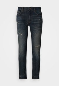 Sötétkék farmernadrág karcsúsított szabással, kopott hatású részekkel és enyhe fakítással. Klasszikus ötféle zsebbel, cipzáros sliccel és gombos rögzítéssel.