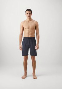 Shorts à cordon bleu marine en tissu léger, dotés d'une ceinture élastique et d'une coupe décontractée, portés par un mannequin masculin torse nu.