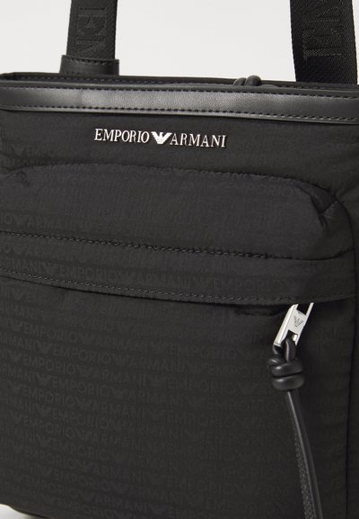 Rucsac negru din nylon cu logo-ul gravat Emporio Armani, textură netedă, buzunar frontal cu fermoar și accente elegante din metal argintiu.