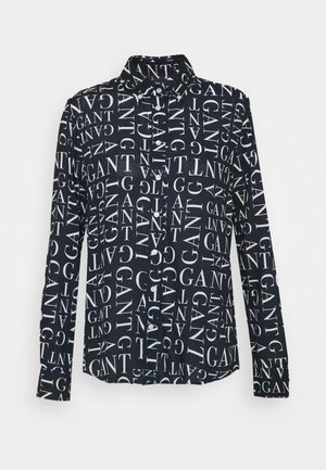 Zwarte blouse met lange mouwen en knopen, geheel bedekt met witte "GANT" tekst in verschillende richtingen.