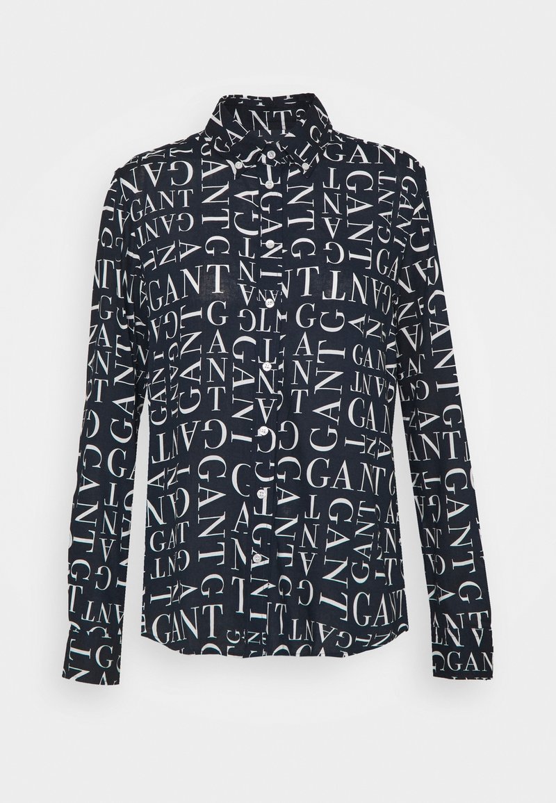 Chemise noire à manches longues boutonnée, entièrement décorée de texte blanc "GANT" dans différentes orientations.