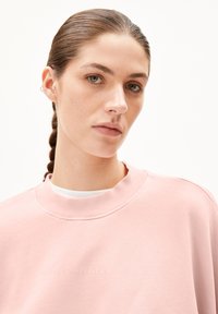 Ljust rosa sweatshirt med rund halsringning, prydd med en subtil blindpräglad logotyp. Tyget ser mjukt ut med en slät textur och avslappnad passform.
