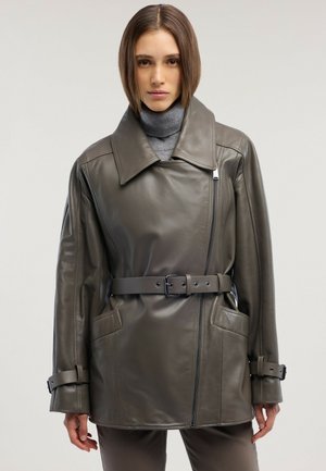 Femme portant une veste en cuir gris foncé ceinturée avec un large col et une fermeture éclair, par-dessus un pull à col roulé gris.