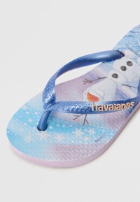 Ciabatte blu con una cinturino testurizzato e una soletta decorata con un design di pupazzi di neve, su uno sfondo che sfuma dal blu al viola.