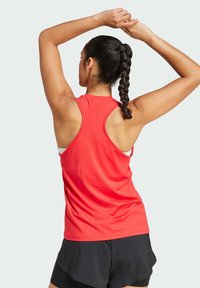 Top atletico rosso con design a schiena scoperta, abbinato a un reggiseno sportivo bianco al di sotto, accompagnato da pantaloni corti neri.