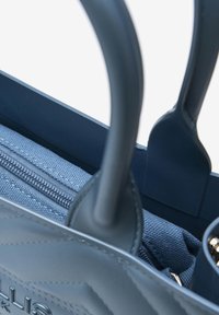 Sac à main bleu avec un extérieur en cuir lisse, comportant une poche zippée, un intérieur en textile et des poignées doubles pour le transport.