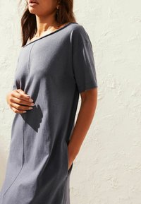 Robe en coton grise avec des manches courtes, coupe décontractée, poches latérales et un col arrondi, présentant une texture lisse et douce.