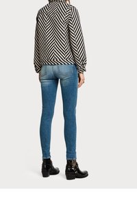 Mustavalkoinen raidoitettu takki korkealla kauluksella, yhdistettynä tiukkoihin sinisiin farkkuihin ja mustiin nilkkureihin, joissa on niittikoristeet.