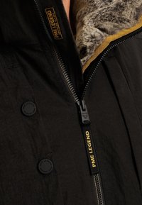 Čierna bunda s golierom z umelého kožušiny, s bočným zapínaním na zips, čiernymi gombíkmi a logom PME Legend na zips a golieri.