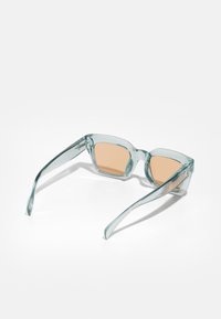 Ochelari de soare cu o ramă transparentă de culoare albastru deschis și lentile de nuanță maronie. Formă pătrată, cu brațe elegante și subțiri, fără hardware vizibil.