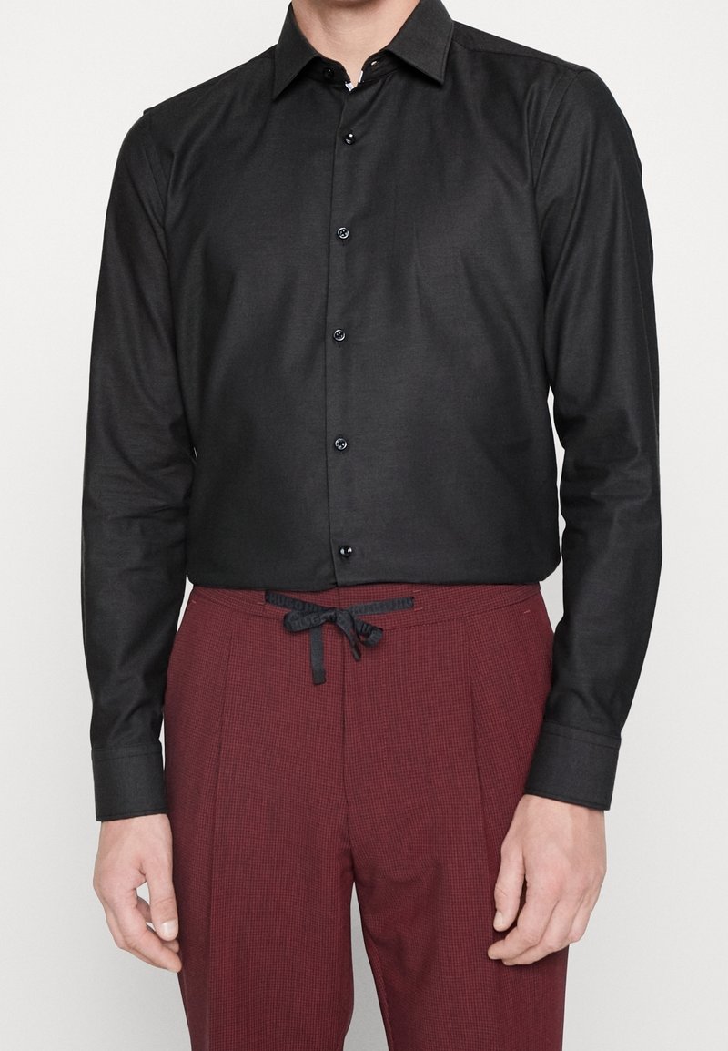 Czarna koszula z długim rękawem, klasycznym kołnierzykiem, zapinana na guziki z gładką fakturą, zestawiona z bordowymi, kratkowymi spodniami z regulowanym sznurkiem w pasie.