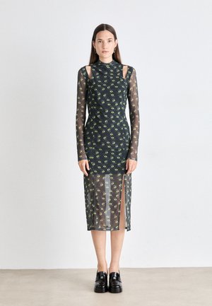 Green eye print midi dress with a high neck, long sheer sleeves, and side slits. Made of lightweight, transparent fabric. Black shoes worn.