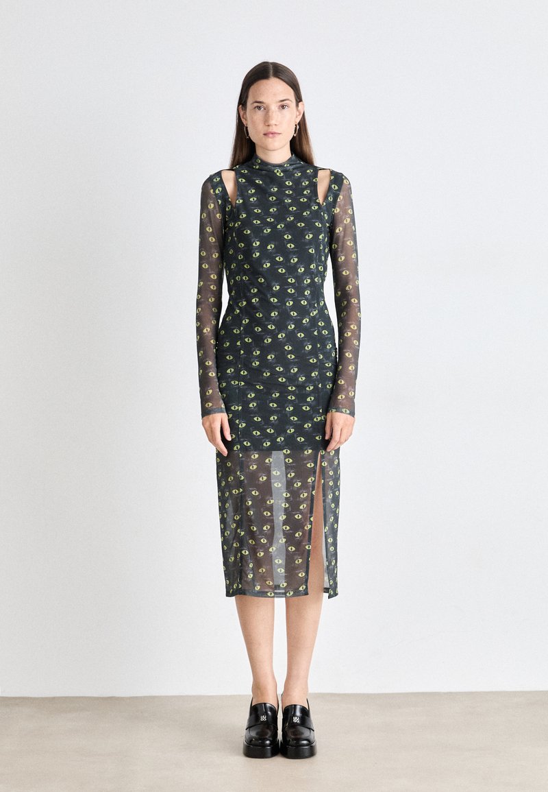 Green eye print midi dress with a high neck, long sheer sleeves, and side slits. Made of lightweight, transparent fabric. Black shoes worn.