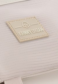 Beige szövet folt, dombornyomott "JOHNNY URBAN" logóval, textúrált szürke háttérre varrva, világos elasztikus részlettel és sima felülettel.