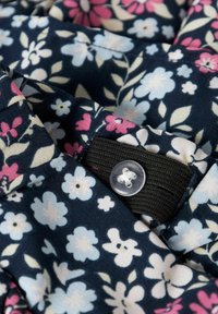Blommigt tyg med olika blommor i nyanser av ljusblått, rosa och vitt på en mörknavy bakgrund, med en klar knapp och svart gummiband.