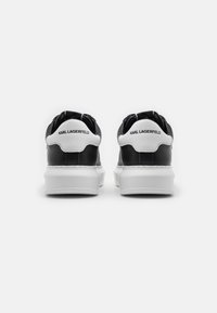Zwart-witte sneakers met een glad leren bovenwerk, gewatteerde kraag, witte tussenzool en branding op de hiel in zwarte tekst.