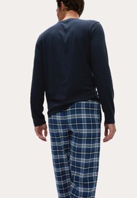Camiseta de manga larga azul marino con cuello redondo, combinada con pantalones de pijama a cuadros azules con líneas blancas, de corte relajado y material suave.