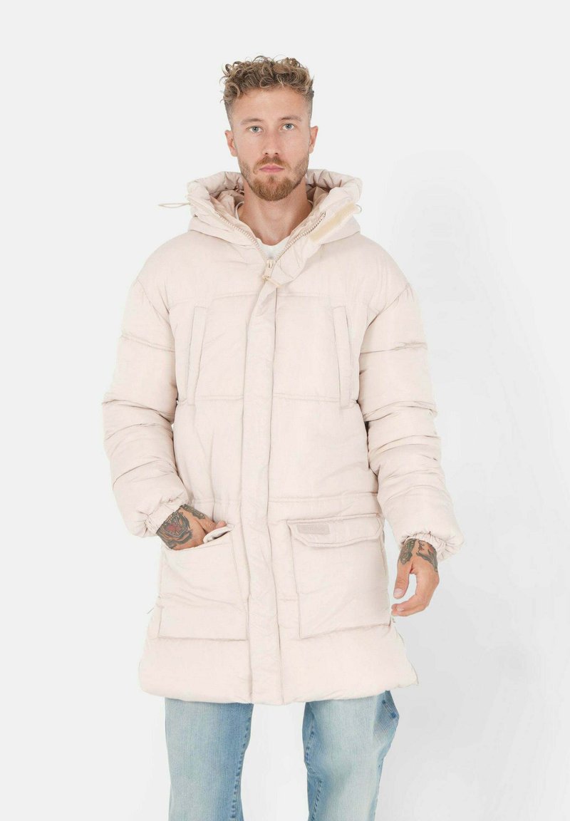 Gevoerde beige jas met een capuchon, voorzien van grote zakken, een ritssluiting aan de voorkant en een relaxte pasvorm. De stof lijkt glad en lichtgewicht.