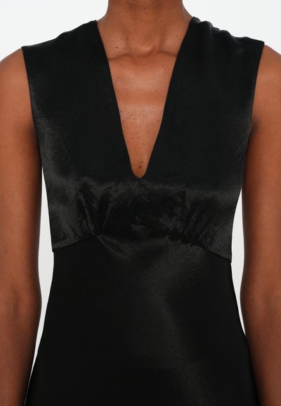 Svart ärmlös klänning med djup V-ringning, samlad midja och slät textur. Tyget har en subtil lyster som framhäver den rena silhuetten.