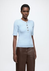 Ανοιχτό μπλε ριμπ κοντομάνικο τοπ με πέντε διακοσμητικά κουμπιά στο μπροστινό μέρος και στρογγυλή λαιμόκοψη. Συνδυασμένο με καφέ δερμάτινο παντελόνι.