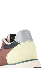 Brown leather sneaker with a gray and green suede heel accent, textured black panel, and cream-colored laces. Logo visible on heel.