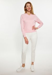 Hellrosa V-Ausschnitt-Pullover mit langen Ärmeln, kombiniert mit weißen Slim-Fit-Hosen und weißen Sneakers. Weicher Stoff, lässiges Design.