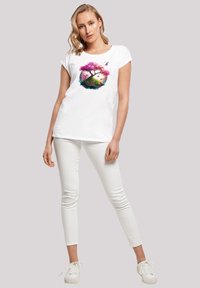Weißes Kurzarm-T-Shirt mit einem bunten Druck eines rosa Baumes und Landschaftsbild. Getragen mit weißen Slim-Fit-Hosen und weißen Schuhen.
