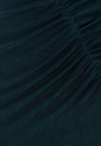 Petrolkleurige stof met een diagonale plooienstructuur, voorzien van een subtiel geribd patroon dat diepte en visuele aantrekkingskracht toevoegt.